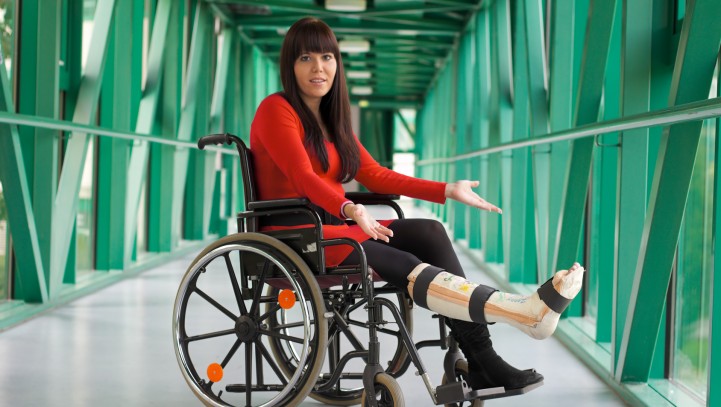 Junge Frau mit Gipsbein sitzt in einem Rollstuhl