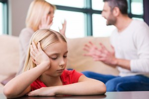 I hope they will work it out. Sad little girl leaning at the table and holding head in hand while her parents shouting at each other in the background